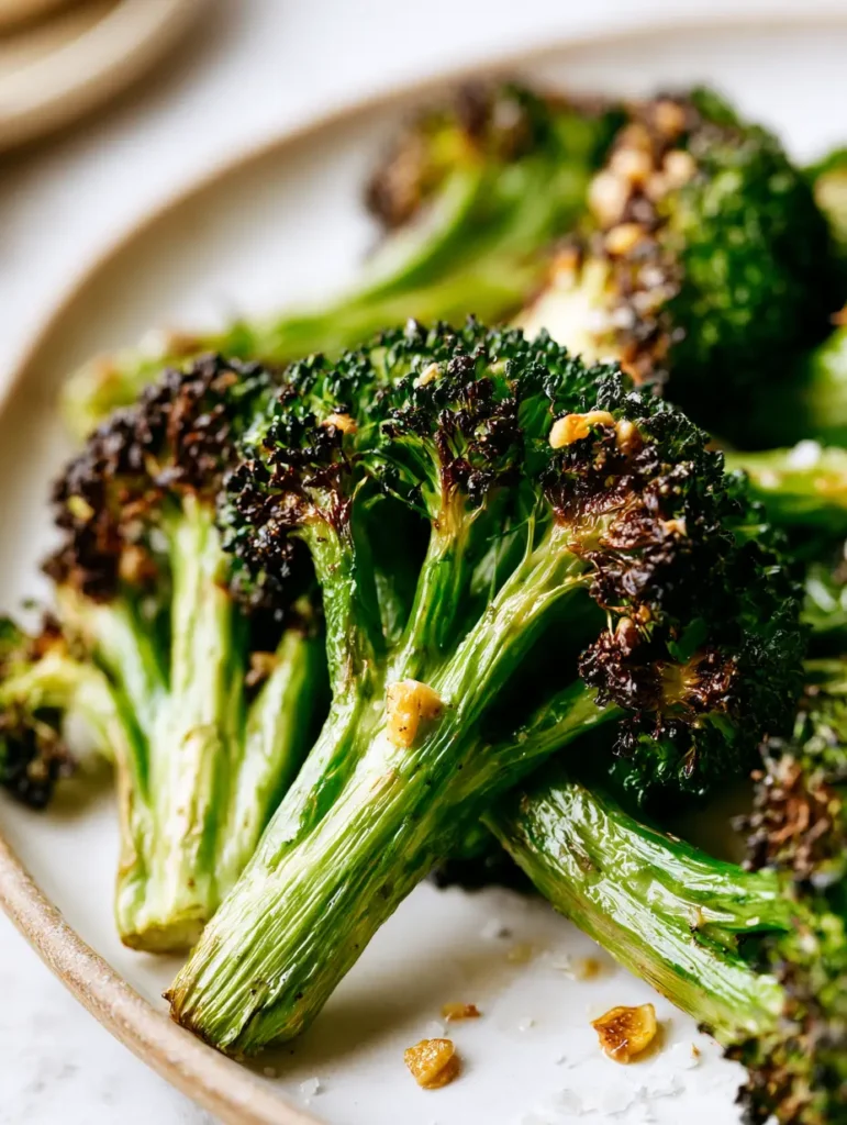 Close up of blistered charred broccoli florets seasoned with coarse salt crystals and garlic. (Air Fryer Broccoli)
