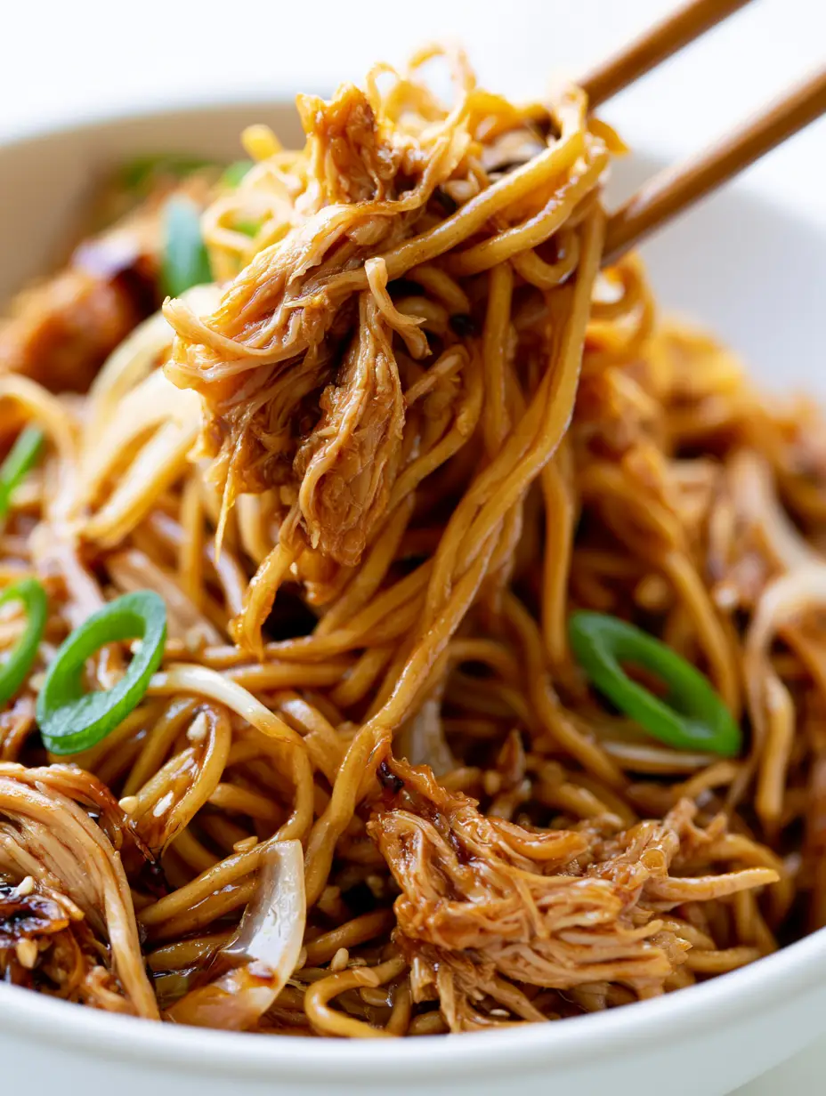 Extreme macro close-up of glossy stir-fry sauce coating thin noodles and shredded chicken. (Chicken Chow Mein Recipe)