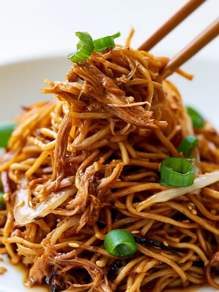 Asymmetrical pile of stir-fried noodles with green scallion circles and charred edges.