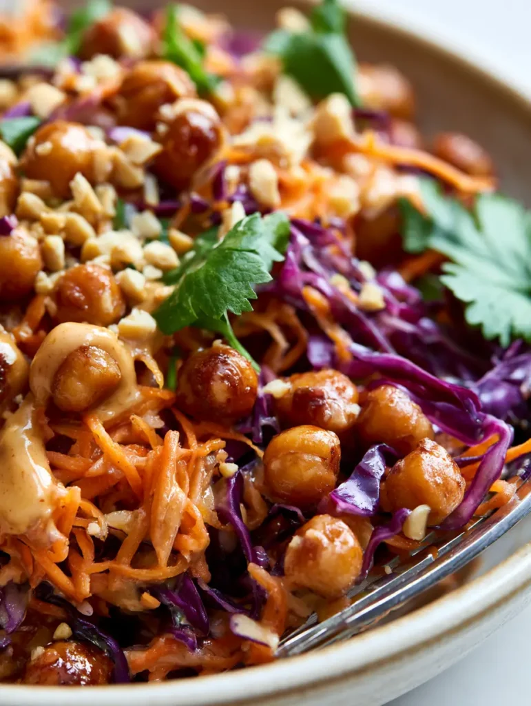 A beautifully messy Thai Chickpea Salad in a ceramic bowl with creamy peanut dressing drips and fresh cilantro.