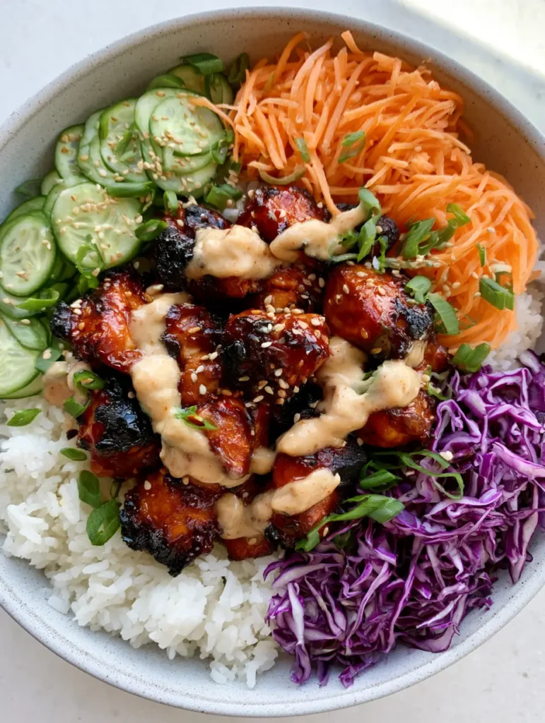 Top-down view of the assembled Korean BBQ Chicken Bowls showing the arrangement of fresh vegetables and sauce.