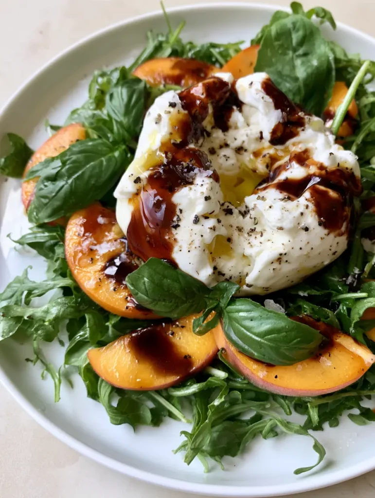Peach Burrata Salad with Balsamic Glaze and Fresh Basil 1 Wide shot of Peach Burrata Salad with fresh basil leaves and cracked black pepper on a neutral background.