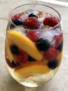 A handheld smartphone photo of a tall glass pitcher and stemless wine glass filled with chilled peach moscato sangria on a stone tabletop.