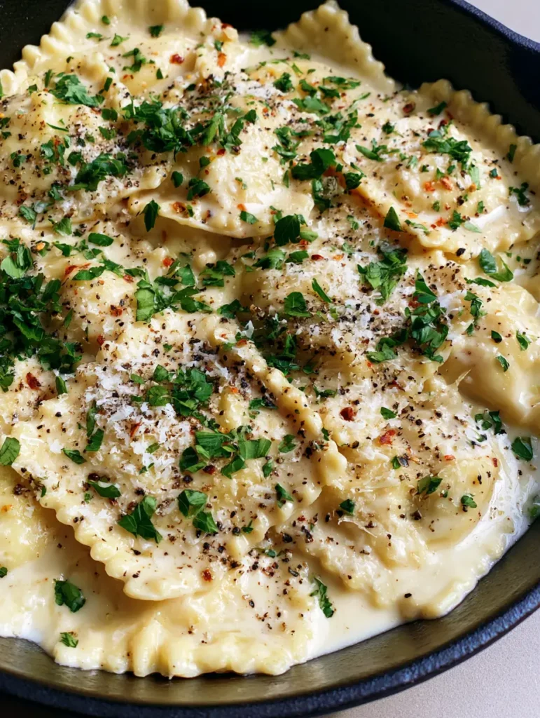 Glossy Garlic Parmesan Ravioli Sauce in a black matte cast iron skillet with coarse black pepper and paprika flakes.