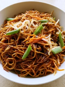 Smartphone photo of a Chow Mein Recipe in a white ceramic bowl showing dark soy glaze and scallions.