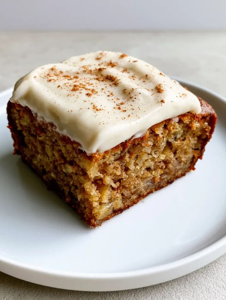 Banana Bread Brownies with Thick Cream Cheese Frosting 1 A square-cut Banana Bread Brownie resting on a white ceramic plate showing caramelized chewy edges and specks of ground cinnamon dusted over the frosting.