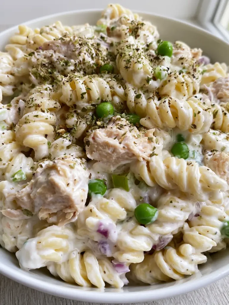 Creamy Chicken Pasta Salad: The Ultimate Easy Potluck Favorite 2 A close-up handheld smartphone photo of a creamy chicken pasta salad served in a white ceramic bowl featuring rotini and peas. (Creamy Chicken Pasta Salad)