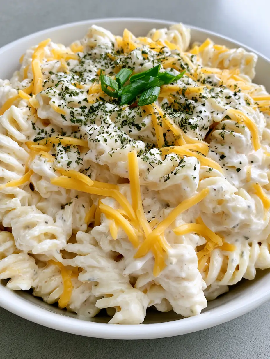 Creamy Cheddar Pasta Salad with Rich Sour Cream Dressing 3 Close up handheld photo of creamy pasta salad with thick ivory dressing and shredded yellow cheddar. (Creamy Cheddar Pasta Salad)