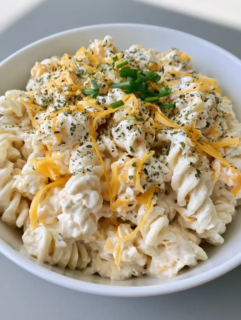 Creamy Cheddar Pasta Salad with Rich Sour Cream Dressing 1 Overhead view of Creamy Cheddar Pasta Salad in a white bowl with chive garnish.