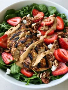 Top-down view of Strawberry Pecan Chicken Salad featuring baby spinach, arugula, sliced grilled chicken breast, and creamy pecan butter vinaigrette.