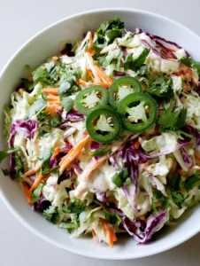 Close-up of fresh Jalapeño Slaw in a white bowl showing the glossy texture of the creamy dressing and vibrant orange julienned carrots.