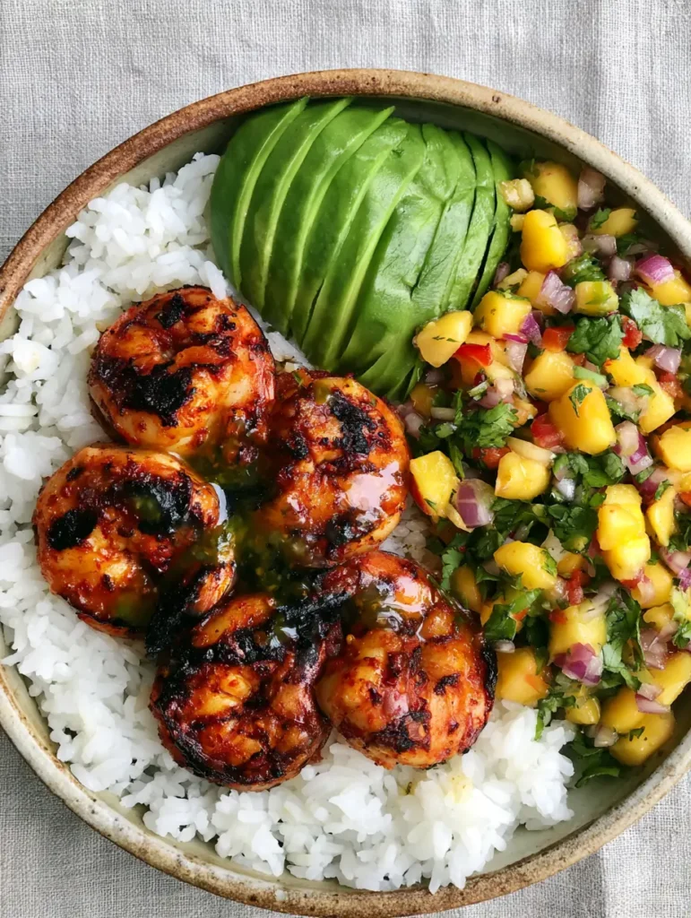 Shrimp and Avocado Bowls with Grilled Chili Shrimp & Mango Salsa 1 A rustic ceramic bowl containing fluffy white jasmine rice, mango cubes, red onion, and sliced avocado.