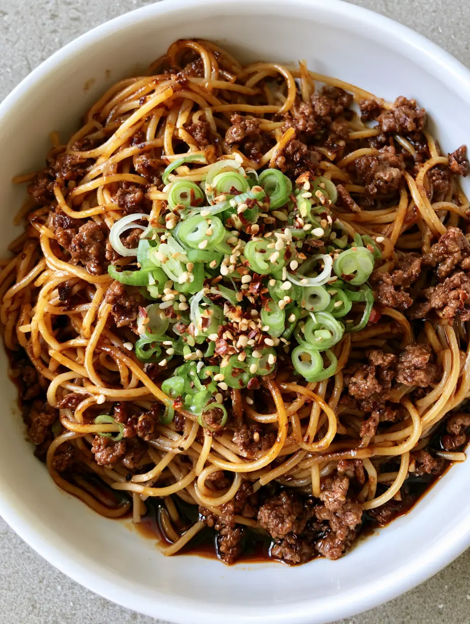 Asian Ground Beef Spaghetti: The Ultimate 20-Minute Glossy Noodle Dinner 4 Handheld photo of a white ceramic bowl filled with Asian Ground Beef Spaghetti, showing the oily sheen and browned beef crumbles.