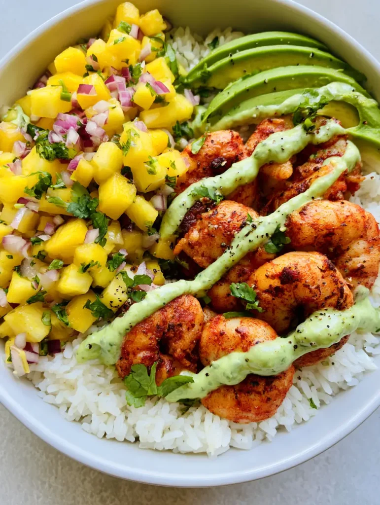 A Tropical Shrimp Rice Bowl topped with a thick pale green avocado crema drizzle in a zig-zag pattern and fresh cilantro.