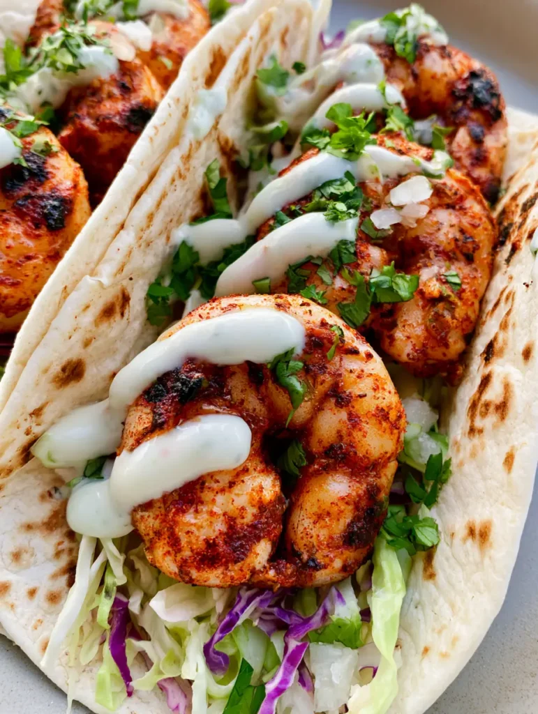 Handheld smartphone shot of three Grilled Shrimp Tacos topped with fresh cilantro and white lime crema.