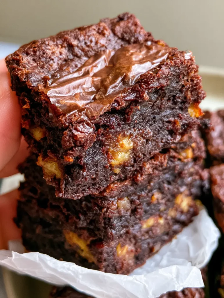 Close up top-down shot of a fudgy banana brownie held in a hand showing dense chocolate crumb. (banana brownies)