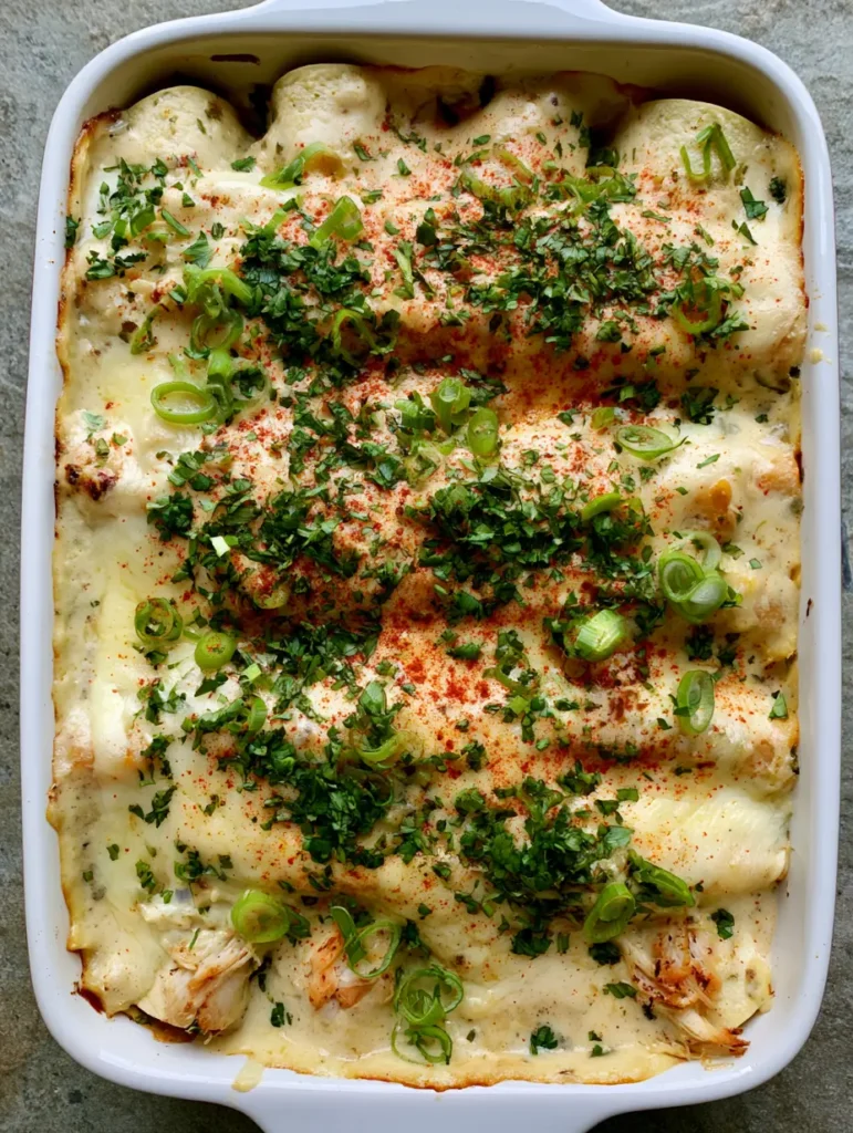 Queso Chicken Enchiladas with Creamy White Sauce 1 Handheld photo of a rectangular dish filled with chicken enchiladas, topped with green scallions and cilantro.