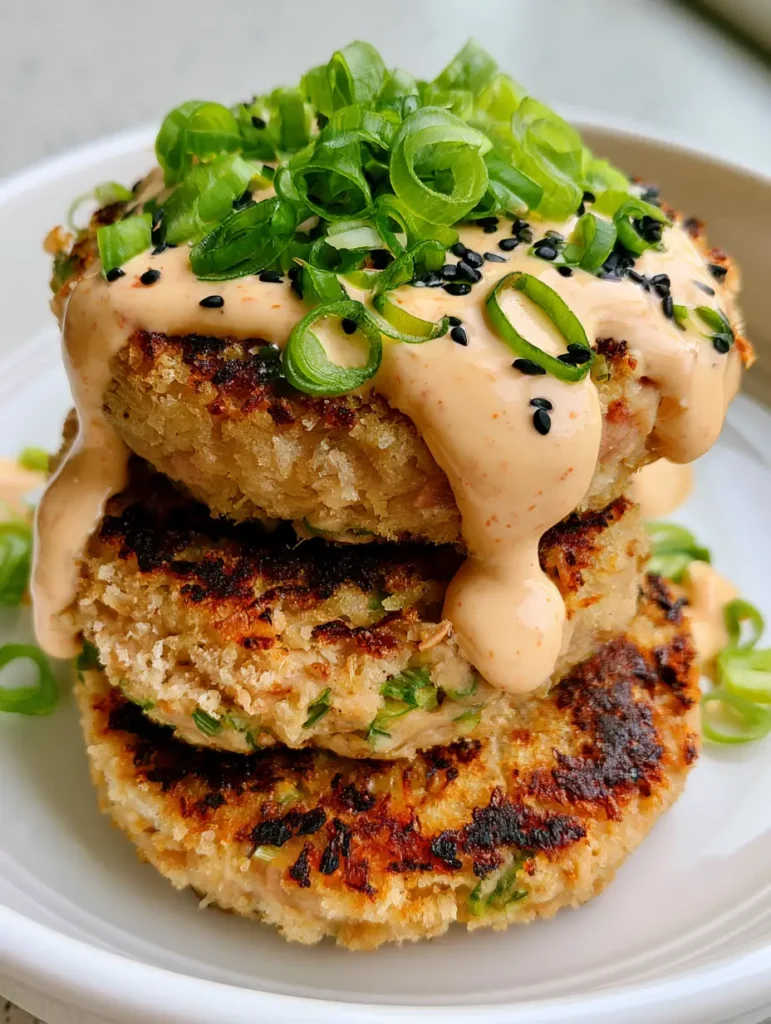 Asian Tuna Cakes stacked on a white ceramic plate with a thick orange sriracha mayo drizzle.