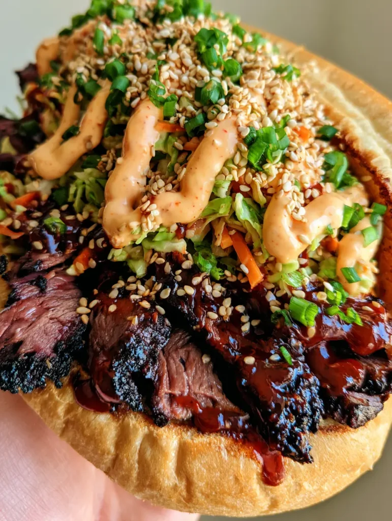 Close-up of a Korean Steak Sandwich held in hand, showing the glossy gochujang glaze and charred beef edges.